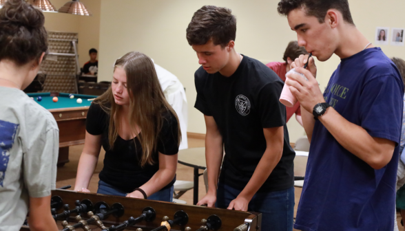 Several play foosball while another looks on