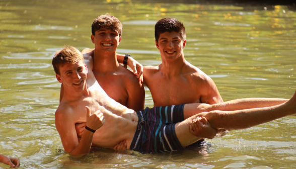 Two hold up a third who gives a thumbs-up