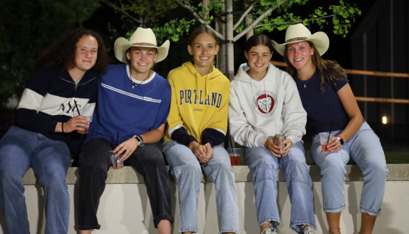 Five sitting on a ledge pose for the camera (two are wearing cowboy hats)