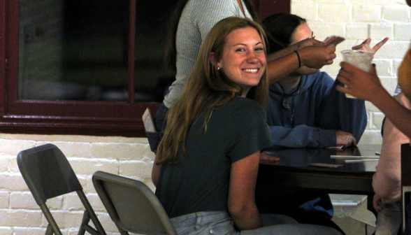 Students play cards at one of the coffee shop tables, and one turns to smile at the camera