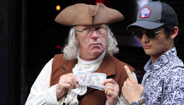 A student poses with an actor dressed as Benjamin Franklin, who is holding a $100 bill (which depicts him)