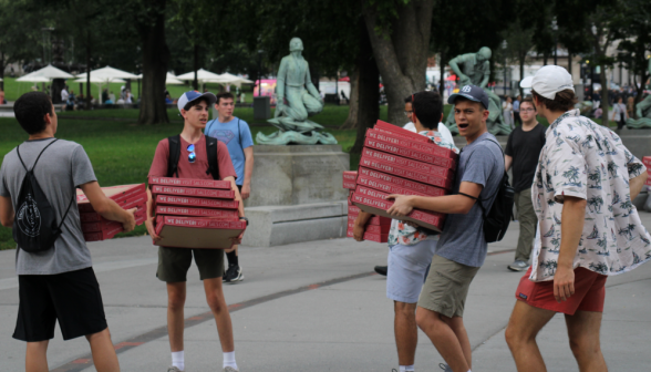 Students carry enormous stacks of pizza