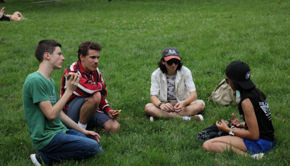 Four eat pizza in a circle on the grass