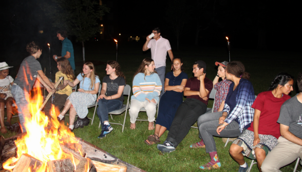 Students laugh and chat around the fire