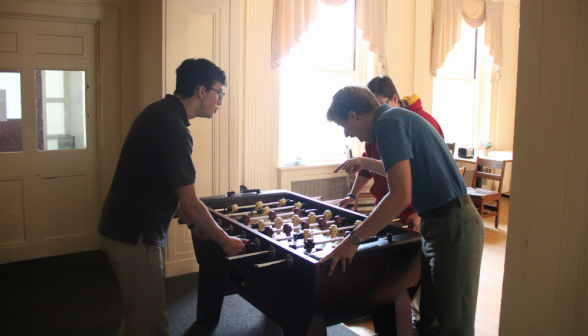 Two play foosball while a third cheers them on