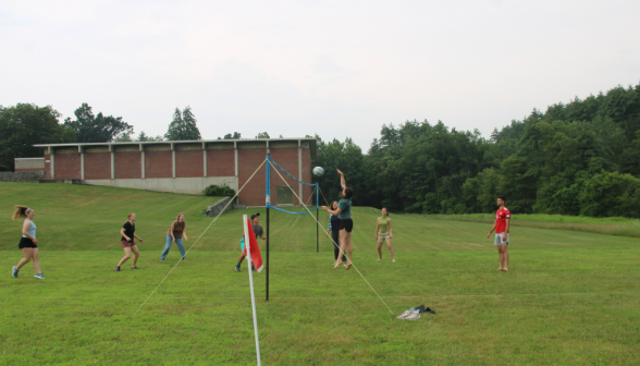 Students play volleyball; one spikes the ball over the net