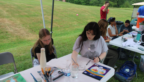 Students draw and paint at shaded outdoor tables