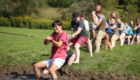 A group of young men and women playing tug of war in the mud.