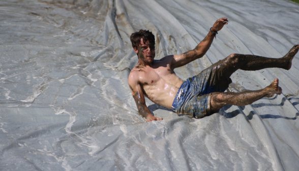 A young man covered in mud lying in the middle of a tarp.