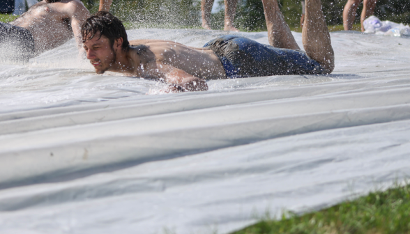 A young man being sprayed in the face while lying face down on a tarp.