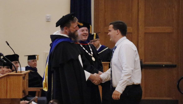 A student shakes hands with the president and president priest