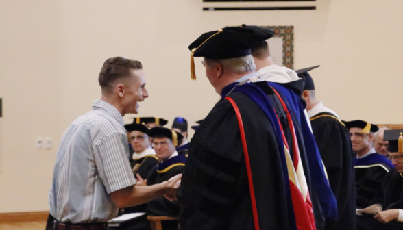 A student shakes hands with the president and presiding priest