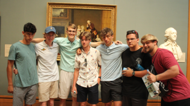 Seven students pose in front of a painting