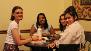 Four girls around a coffee shop table smile for the camera