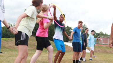 Students hand in hand in a long row try to pass a hula hoop along without breaking the chain