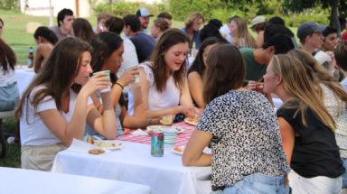 Students at picnic tables enjoy the BBQ