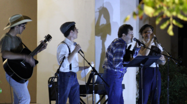 An open mic night performance: one plays the guitar and three sing