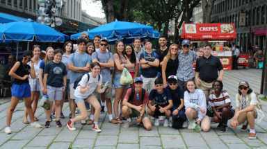 The students pose as a group afront picnic tables and a crepe stand