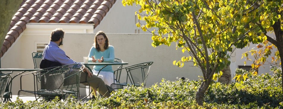 Two people sitting at a table outside by a tree