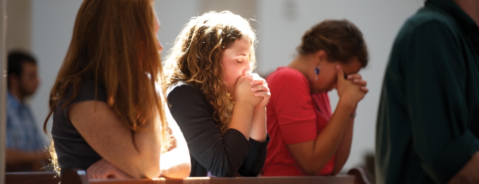 Three people kneeling on a pew praying