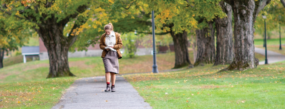 Woman walking down a cement path with trees behind her