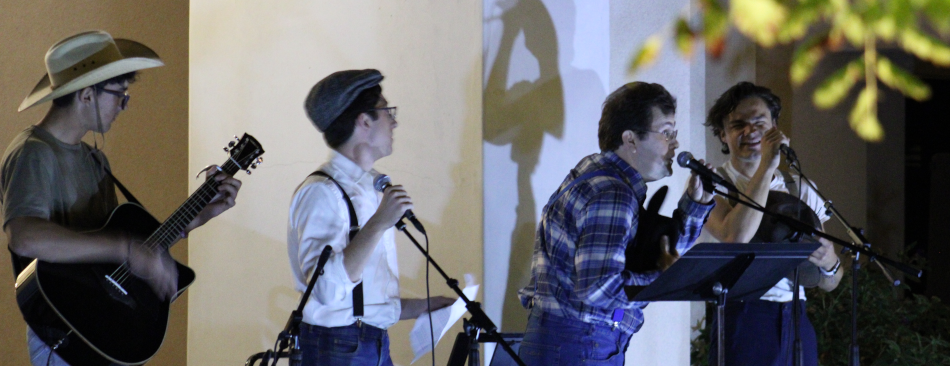 An open mic night performance: one plays the guitar and three sing